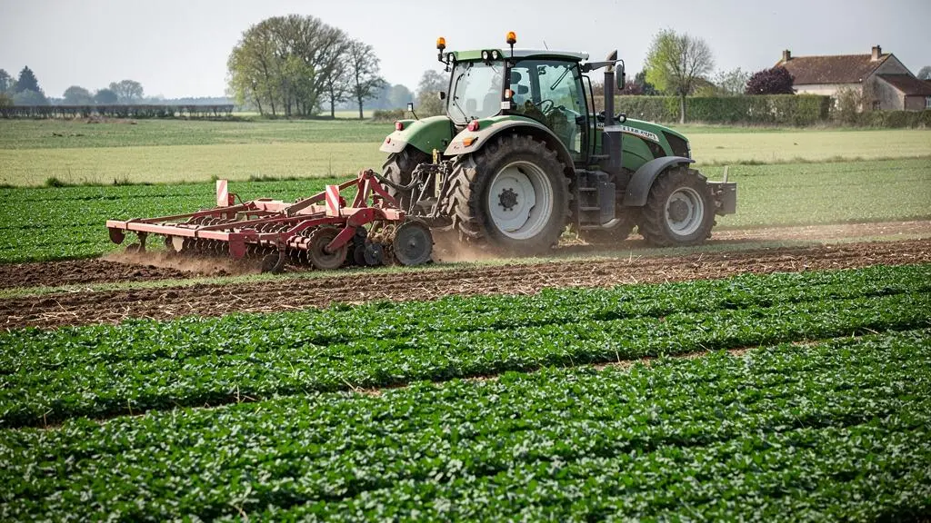 Agricultural tractor with strip-till equipment working in a field, creating narrow tilled bands while preserving cover crop strips